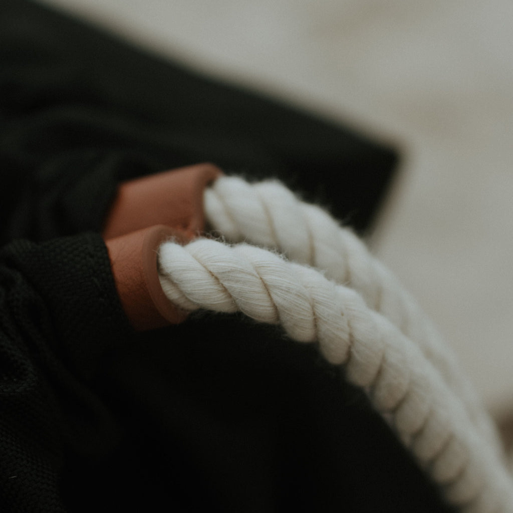 Close-up of a white rope on black oversized backpack with brown leather clip