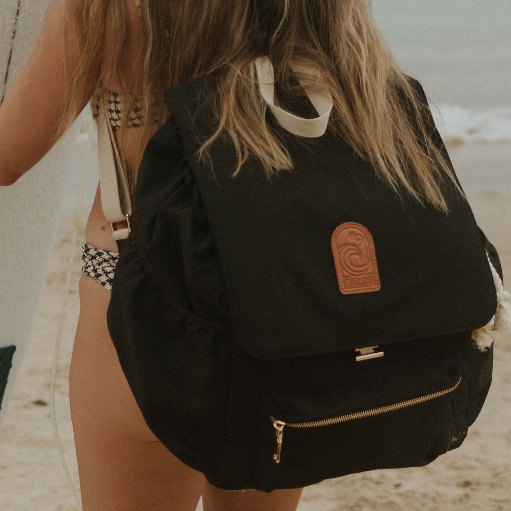 Person on a beach wearing a black backpack with a brand logo.