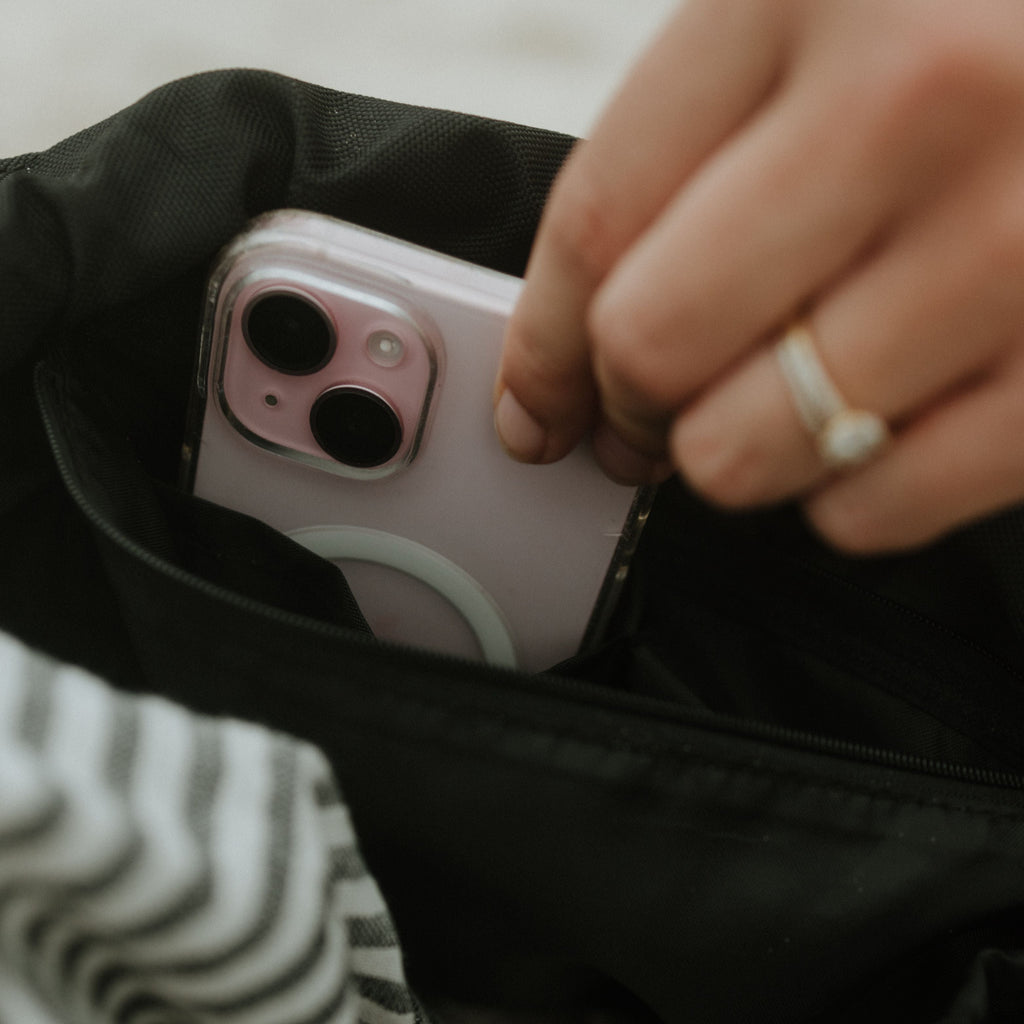 Person placing a smartphone into a black bag with a striped fabric background