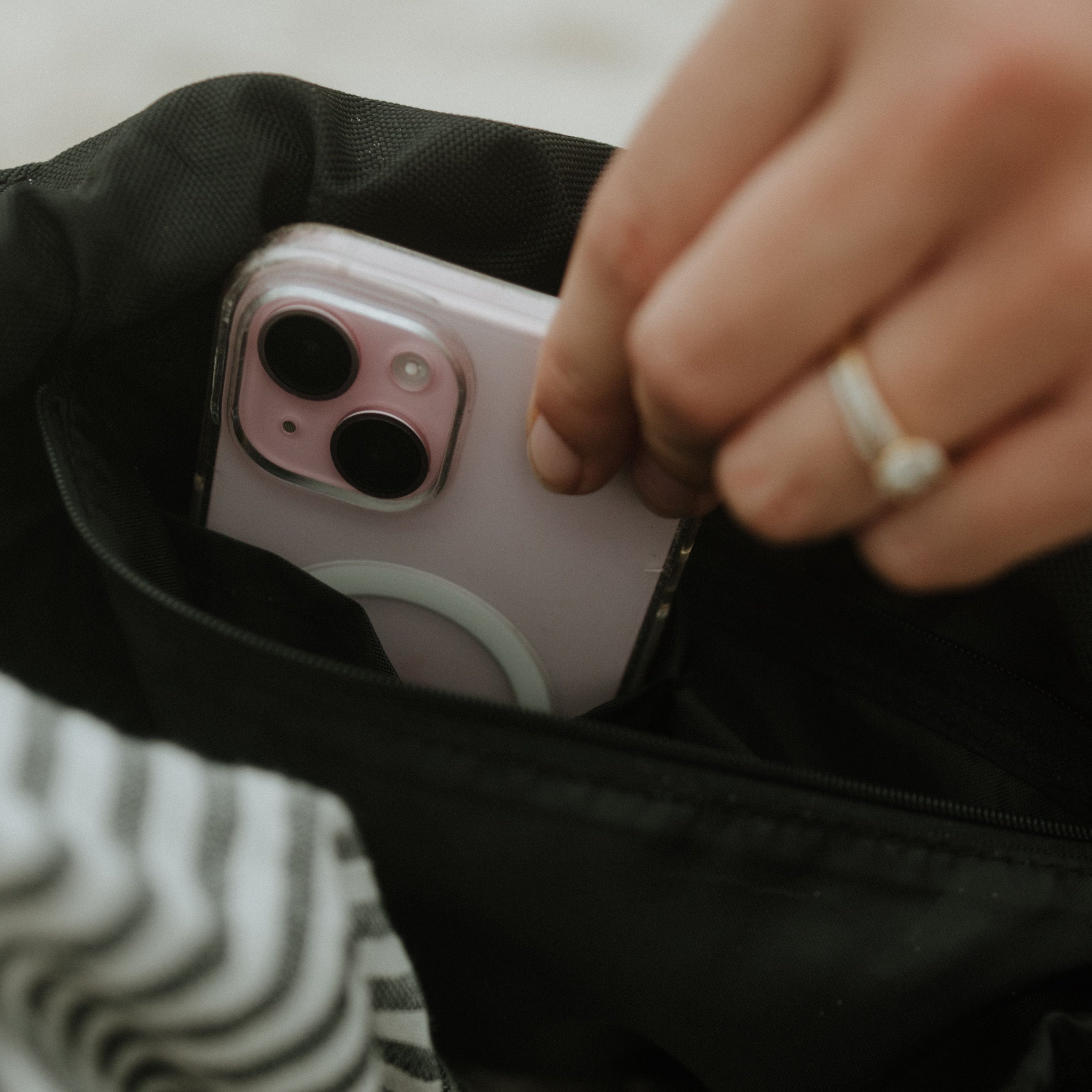 Person placing a smartphone into a black bag with a striped fabric background