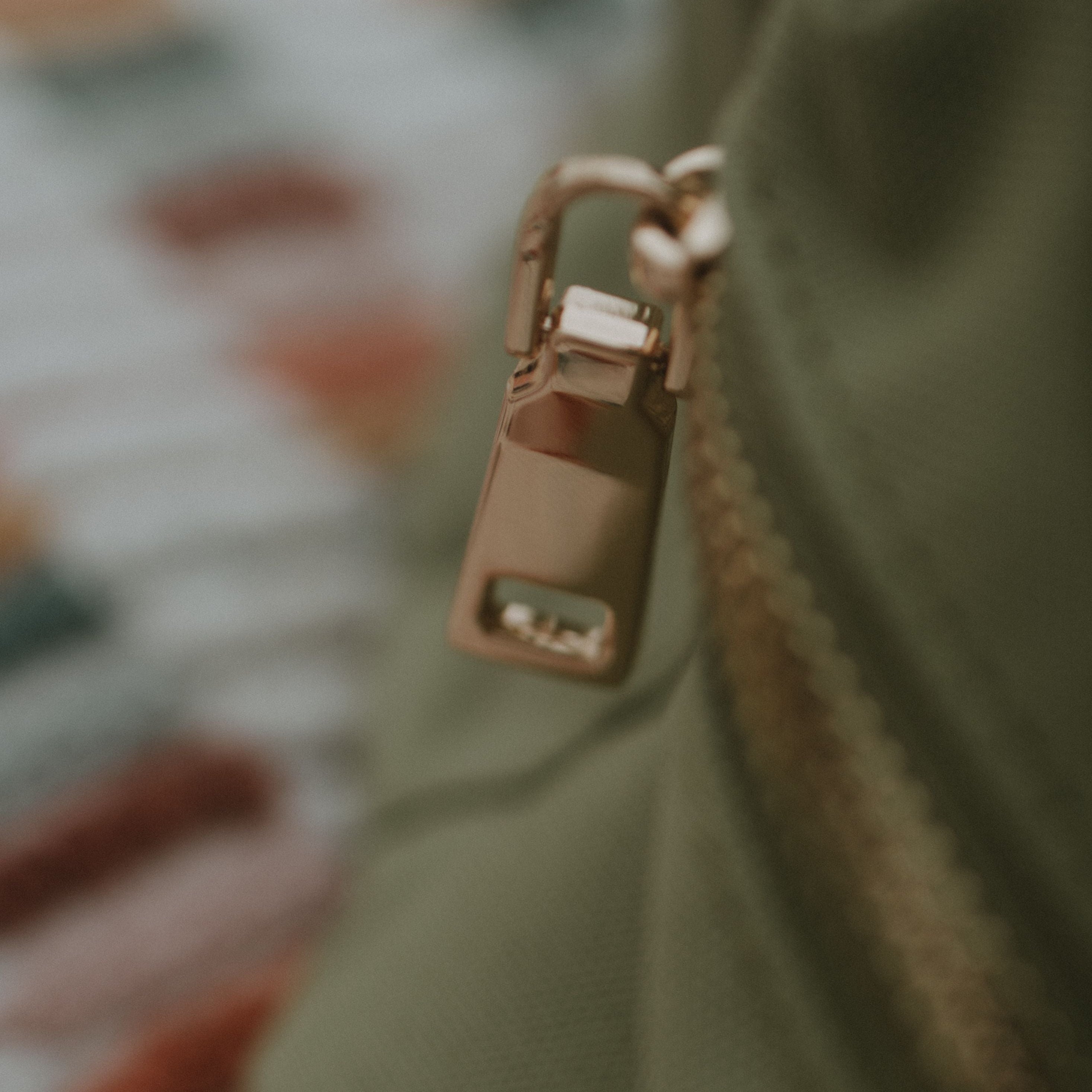 Close-up of a gold zipper pull on a sage fabric background