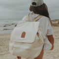 Person with a beige oversized backpack walking on a beach