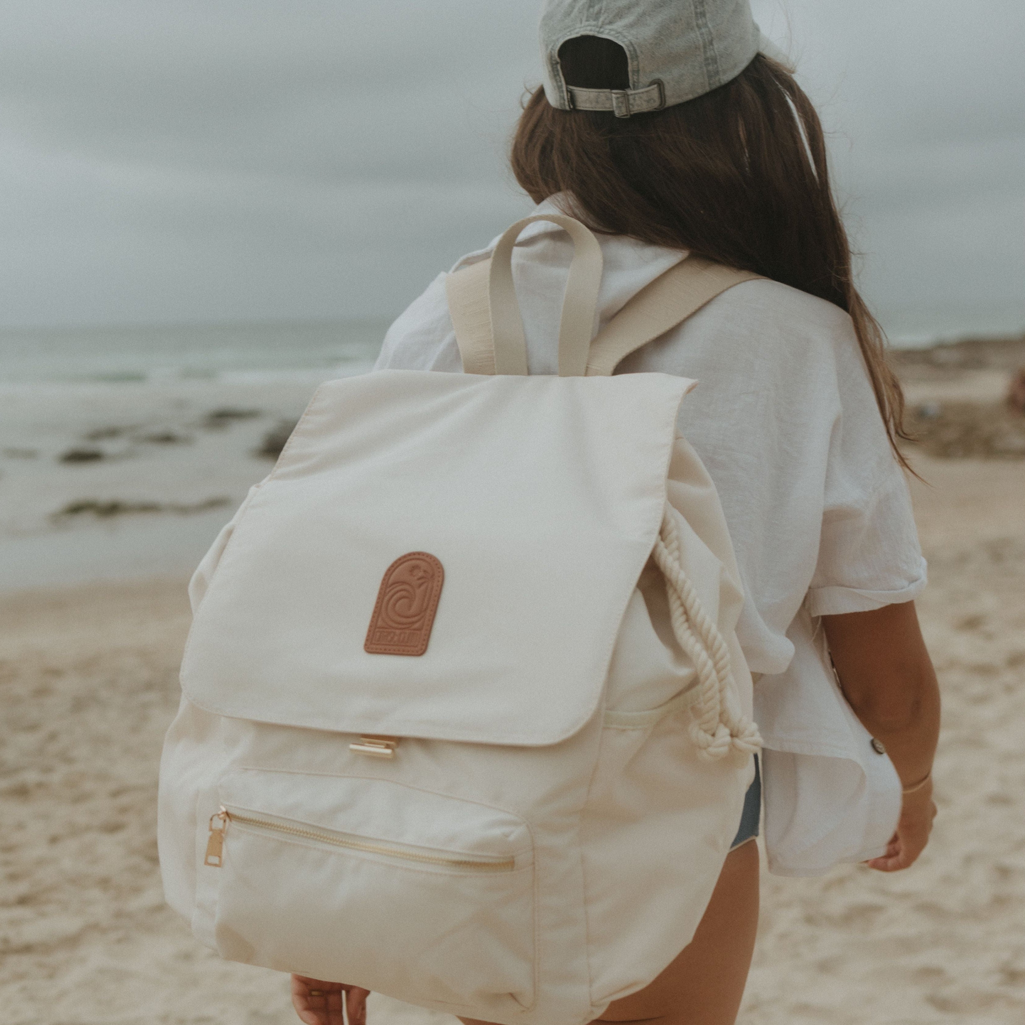 Person with a beige oversized backpack walking on a beach