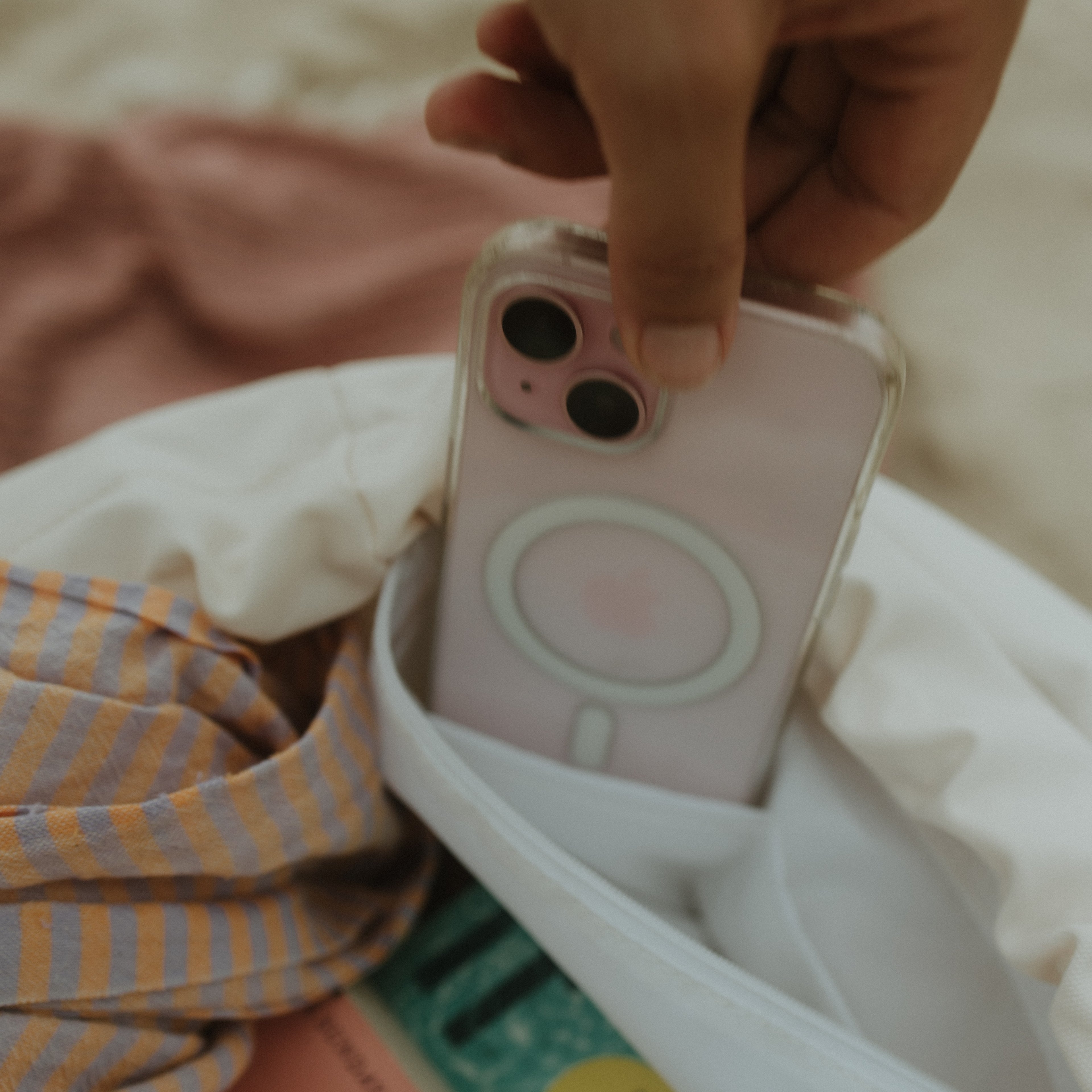 Person holding a phone with a pink case being put into the internal pocket of beige backpack