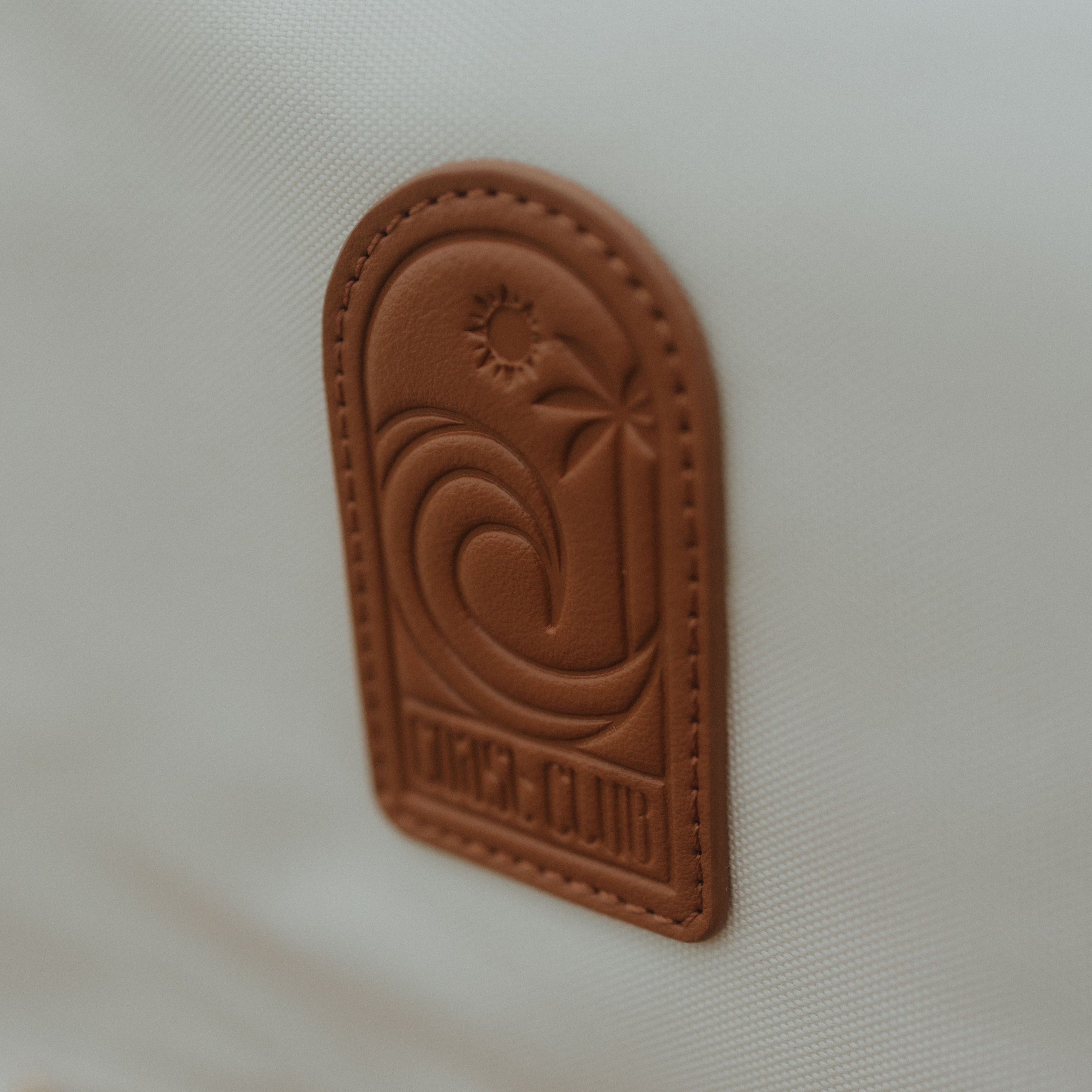 Brown leather patch with embossed design on a beige oversized backpack